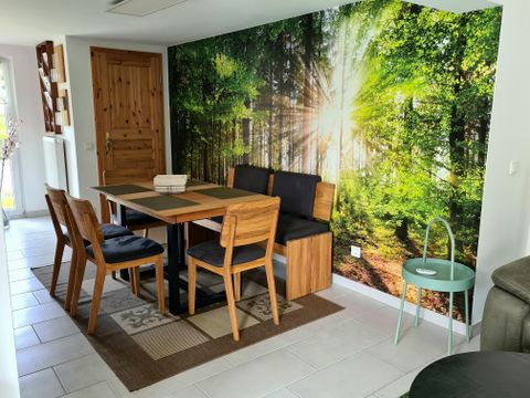 Ein gemütlicher Essbereich mit Holzstühlen und einem Tisch. Die Wand ist mit einem Bild von einem sonnigen Wald dekoriert.