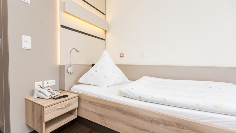 Ein einfaches Schlafzimmer mit einem Einzelbett und einem Nachttisch. Die Wände sind in neutralen Farben gehalten und es gibt eine sanfte Beleuchtung.
