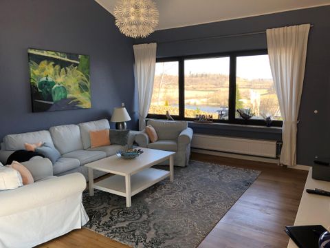 Ein einladendes Wohnzimmer mit bequemen Sofas und einem hellen Tisch. Große Fenster bieten einen Blick auf die Landschaft draußen.