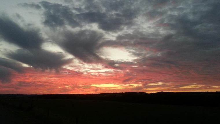 Ein schöner Sonnenuntergang mit leuchtend roten und orangefarbenen Wolken. Der Himmel ist von einer dramatischen Wolkenlandschaft umgeben.