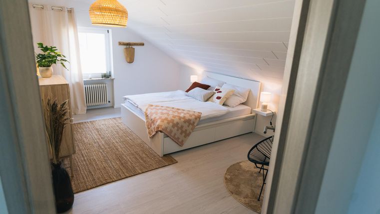 Ein helles Schlafzimmer mit einem großen Bett und gemütlicher Dekoration. Der Raum hat eine freundliche Atmosphäre und einen schönen Teppich.