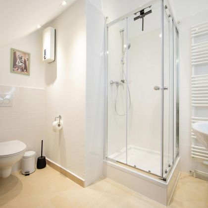 Ein modernes Badezimmer mit einer Dusche aus Glas, einem Waschbecken und einer Toilette. Die Wände sind hell und der Raum wirkt sauber und freundlich.