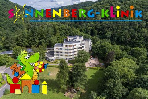 Ein modernes Gebäude der Sonnenberg-Klinik umgeben von grüner Natur. Im Vordergrund ist ein farbenfrohes Kinderlogo zu sehen.