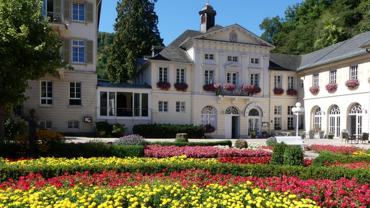 Ein malerisches Gebäude umgeben von bunten Blumenbeeten. Die Atmosphäre ist einladend und ruhig.