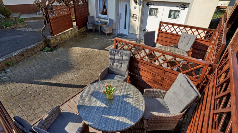 Ein gemütlicher Patio mit einem runden Tisch und bequemen Stühlen. Die Holzverkleidung und die Umgebung schaffen eine einladende Atmosphäre.