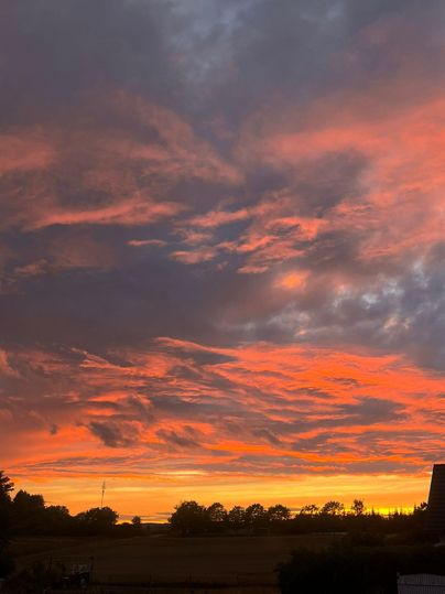 Ein wunderschöner Sonnenuntergang mit leuchtend orangefarbenen und pinken Wolken. Die Landschaft im Vordergrund ist silhouettiert und bietet einen ruhigen Ausblick.