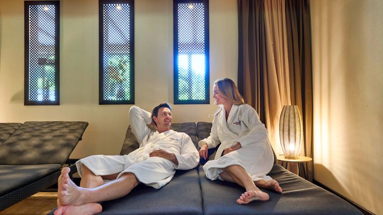 Ein Paar in Bademänteln entspannt in einem modernen Wellnessbereich. Die Atmosphäre ist beruhigend mit sanftem Licht und stilvollem Dekor.