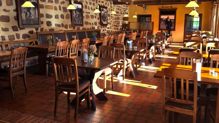Een gezellig restaurant met houten stoelen en -tafels. Zonnelicht stroomt door de ramen en verlicht de ruimte.