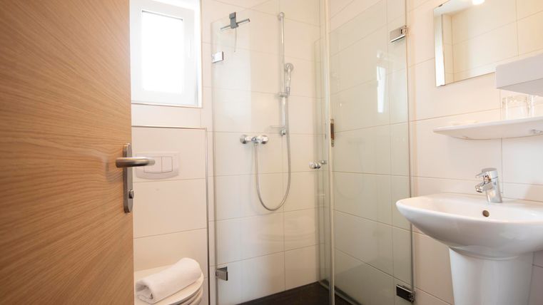 Ein modernes Badezimmer mit einer Dusche, einem Waschbecken und einem WC. Die Wände sind hell gefliest, und es gibt ein Fenster für Tageslicht.