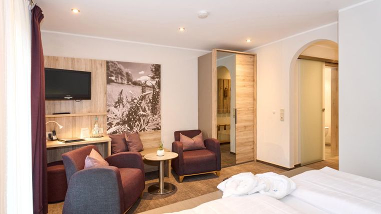 Ein modernes Hotelzimmer mit zwei Betten und einem Sitzbereich. Die Wände sind hell, und es gibt einen Fernseher sowie einen Blick auf ein dekoratives Bild.
