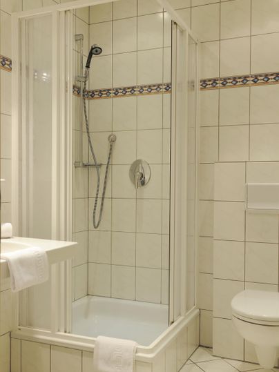 Ein modernes Badezimmer mit einer Duschkabine und einem WC. Die Wände sind mit weißen Fliesen gefliest.