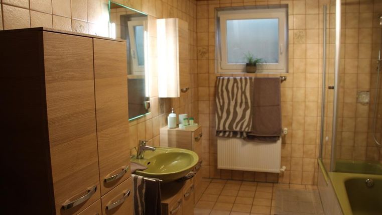 Ein modernes Badezimmer mit Holzmöbeln und einer grünen Waschbecken. Es gibt ein Fenster, eine Dusche und dekorative Handtücher.
