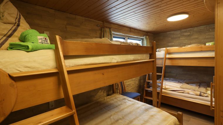 Ein einfaches Zimmer mit zwei Etagenbetten aus Holz. Die Wände sind hell und der Raum hat eine gemütliche Atmosphäre.