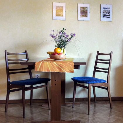 Ein kleiner Tisch mit zwei Stühlen ist im Raum dekoriert. In der Mitte steht eine Obstschale mit Früchten und einer vase mit Blumen.