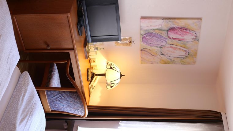 Ein gemütlicher Raum mit einem Tisch, einem Fernseher und einer Lampe. An der Wand hängt ein abstraktes Gemälde in sanften Farben.