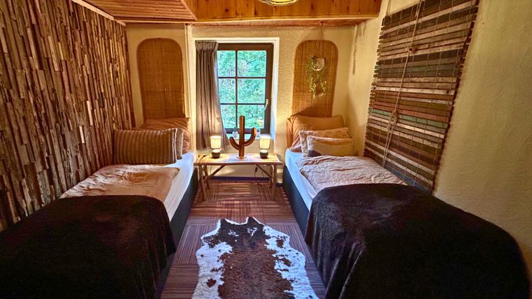 Ein gemütliches Schlafzimmer mit zwei Einzelbetten und einem Holz-Lampenbild. Wände sind mit natürlichen Materialien dekoriert und ein Fenster sorgt für viel Tageslicht.