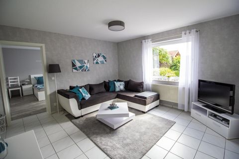 Ein modernes Wohnzimmer mit einem großen Sofa und eleganten Dekorationen. Ein Fenster sorgt für viel Tageslicht und eine angenehme Atmosphäre.