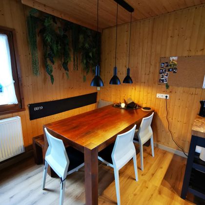 Ein stilvoller Esstisch aus Holz mit weißen Stühlen in einem gemütlichen Raum. Grüne Pflanzen und warmes Licht sorgen für eine einladende Atmosphäre.