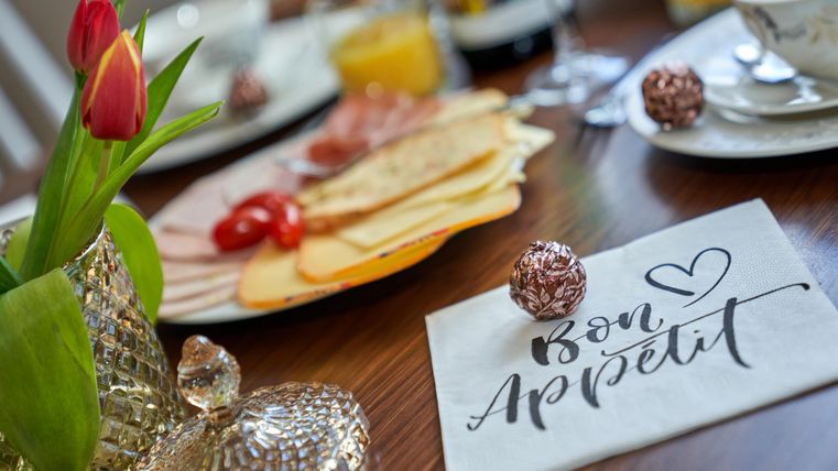 Ein festlich gedeckter Tisch mit verschiedenen Leckereien. Eine Karte mit der Aufschrift "Bon Appétit" und frische Blumen runden das Bild ab.