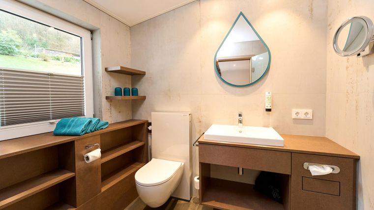 Ein modernes Badezimmer mit einem schlichten Design. Es verfügt über ein Waschbecken, eine Toilette und Regale aus Holz.