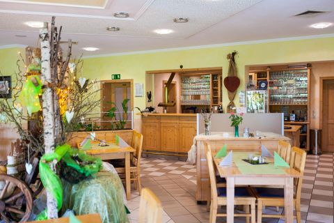 Ein einladendes Restaurant mit Holztischen und einem hellen, freundlichen Ambiente. Pflanzen und Dekorationen sorgen für eine gemütliche Atmosphäre.