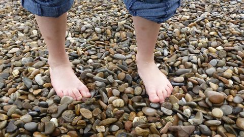 Zwei nackte Füße auf einem Kieselstrand.