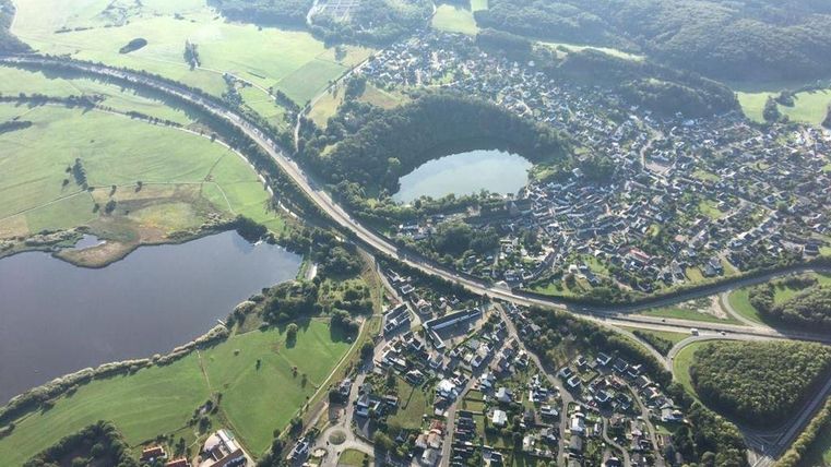 Eine Luftaufnahme einer malerischen Landschaft mit mehreren kleinen Seen und einer Stadt. Die Umgebung besteht aus grünen Feldern und Hügeln.