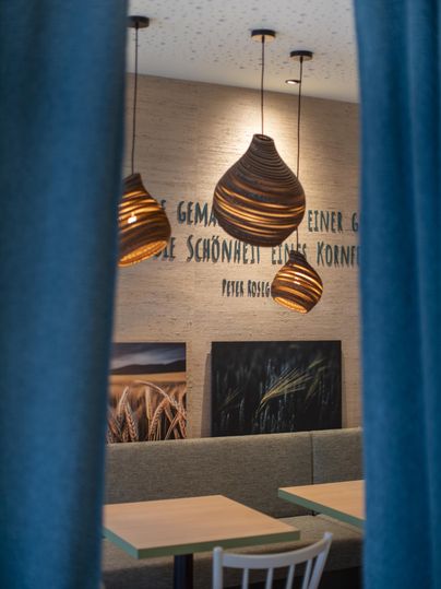 Ein gemütlicher Raum mit Holzpendelleuchten und einer neutralen Wandfarbe. Tische und Stühle laden zum Verweilen ein.