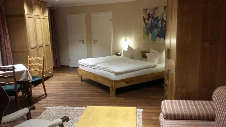 Ein gemütliches Zimmer mit einem Doppelbett, einem Tisch und Stühlen. Die Einrichtung ist Holzmöbel und es gibt ein farbenfrohes Kunstwerk an der Wand.