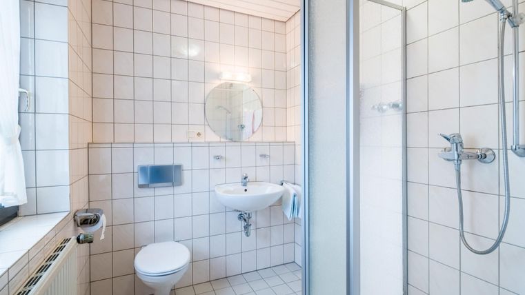 Ein modernes Badezimmer mit weißen Fliesen und einer Duschkabine. Es gibt ein Waschbecken, eine Toilette und einen großen Spiegel.