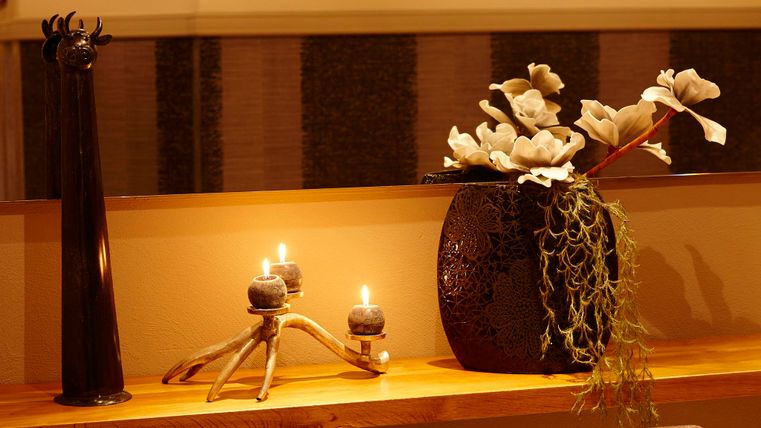 Ein stilvoller Raum mit einer langen Holztischfläche, dekoriert mit Blumen und Kerzen. Im Hintergrund sind dekorative Tierköpfe an der Wand zu sehen.