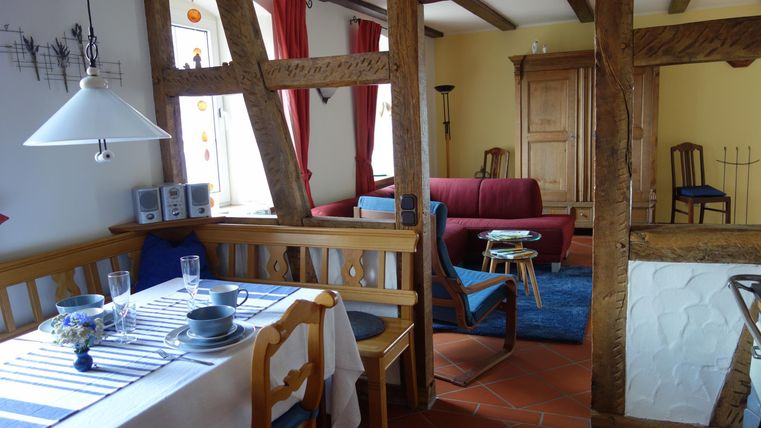Eine gemütliche Wohnküche mit einem Esstisch und Stühlen. Im Hintergrund sind ein rotes Sofa und ein blaues Teppich zu sehen.