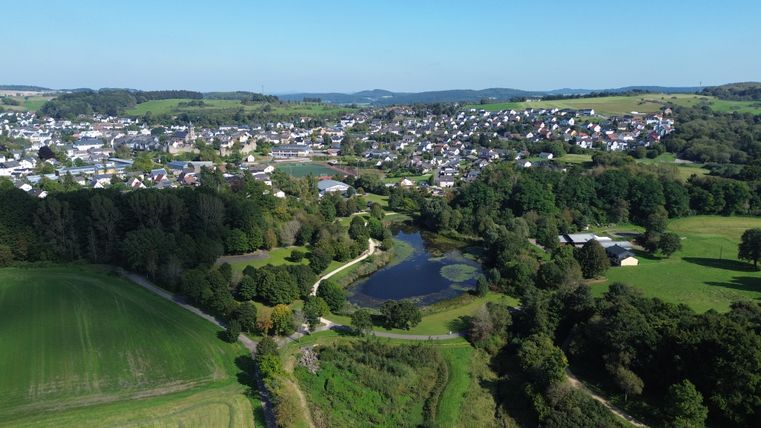 Luftaufnahme der Stadt Hillesheim mit dem kleinen See im Bosldorfer Tälchen und umliegenden Wäldern und Feldern.