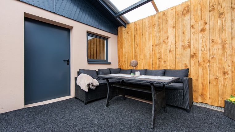 Ein gemütlicher Außenbereich mit einer modernen Sitzgruppe und einem Tisch. Eine Holzwand sorgt für Privatsphäre und Schutz.
