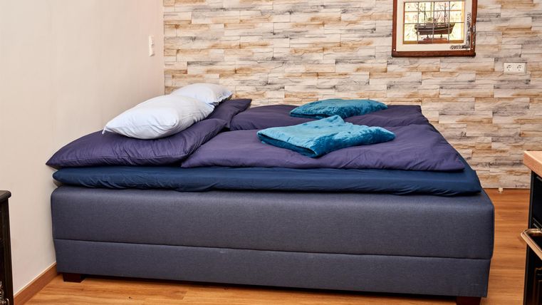 Ein bequemes Bett mit blauen Kissen und einer modernen Holzoptik-Wand. Der Raum hat einen warmen, einladenden Charakter.