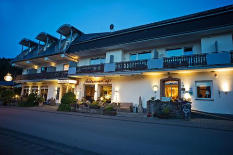 Ein gemütliches Hotelgebäude am Abend mit warmem Licht. Es hat einen einladenden Eingang und eine schöne Fassade.