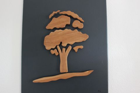Eine Holzskulptur eines Baumes auf einer schwarzen Fläche. Der Baum hat eine stilisierte Form mit flauschigen Blättern und einem stabilen Stamm.