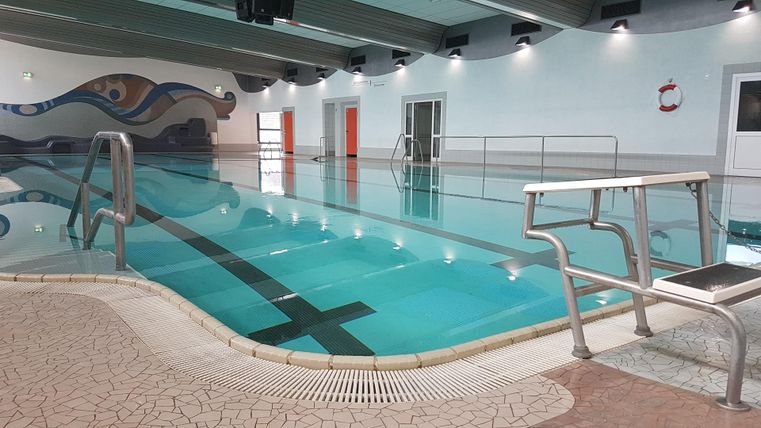 Ein modernes Hallenbad mit klarem Wasser und einer breiten Treppe. Die Wände sind in hellen Farben gestaltet und es gibt Sicherheitsausrüstung in der Nähe.