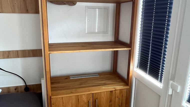 Ein moderner Holzregal mit offenen Regalböden und einer Schublade. Handtücher liegen ordentlich auf dem obersten Regal.