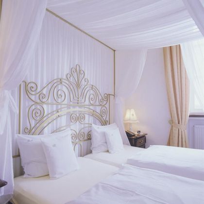 Ein elegantes Schlafzimmer mit zwei Einzelbetten und einem kunstvollen Kopfteil. Der Raum ist hell und freundlich, mit sanften Vorhängen und einer warmen Beleuchtung.