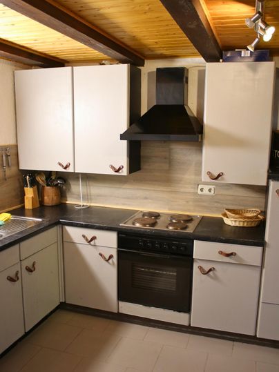 Eine moderne Küche mit weißen Schränken und einem schwarzen Herd. Die Holzdecke verleiht der Küche eine gemütliche Atmosphäre.