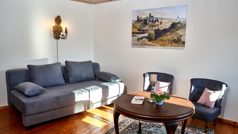 Ein gemütlicher Wohnraum mit einem grauen Sofa und zwei blauen Stühlen. Auf dem Tisch steht eine kleine Blumenvase und ein Bild hängt an der Wand.