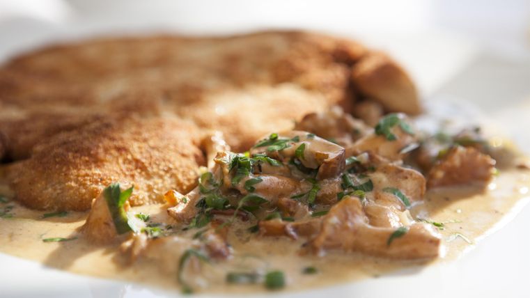 Ein köstliches Gericht mit einer knusprigen Panade und einer cremigen Pilzsauce. Das Essen ist mit frischen Kräutern garniert.