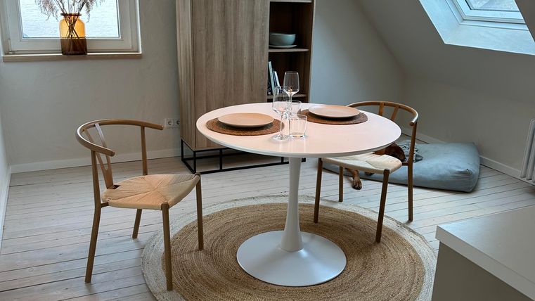 Ein gemütlicher Essbereich mit einem runden Tisch und zwei Stühlen. Das Fenster sorgt für viel Tageslicht und die Dekoration ist minimalistisch gehalten.