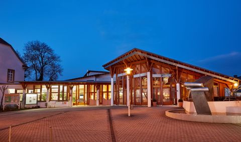 Ein modernes Gebäude mit Holzstruktur und großen Fenstern. Der Himmel ist dunkelblau, was eine ruhige Atmosphäre schafft.