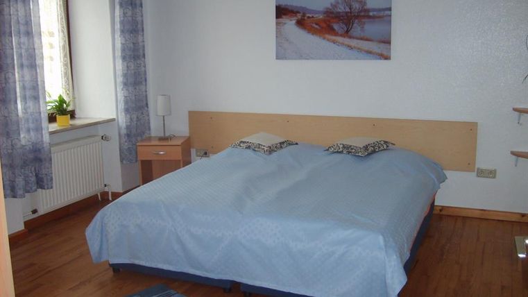 Ein gemütliches Schlafzimmer mit einem großen Doppelbett und hellen Vorhängen. An der Wand hängt ein Bild einer winterlichen Landschaft.