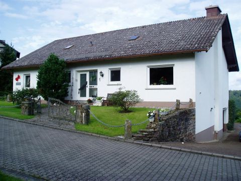 Ein modernes Haus mit einem Mauerzaun und gepflegtem Garten. Die Fassade ist hell und die Umgebung ist grün.