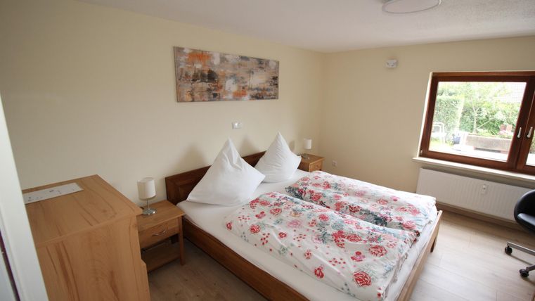 Ein gemütliches Schlafzimmer mit einem Doppelbett und bunten Bettdecken. Es gibt einen Schreibtisch und einen großen Fensterblick nach draußen.