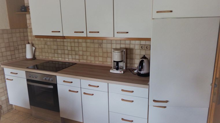 Eine moderne Küche mit weißen Schränken und einer dunklen Arbeitsplatte. Es gibt einen Herd, eine Kaffeemaschine und eine elegante Wasserkocher.