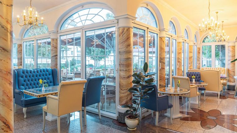 Ein stilvolles Restaurant mit großen Fenstern und eleganten Möbeln. Die hellen Farben und die charmante Einrichtung schaffen eine angenehme Atmosphäre.